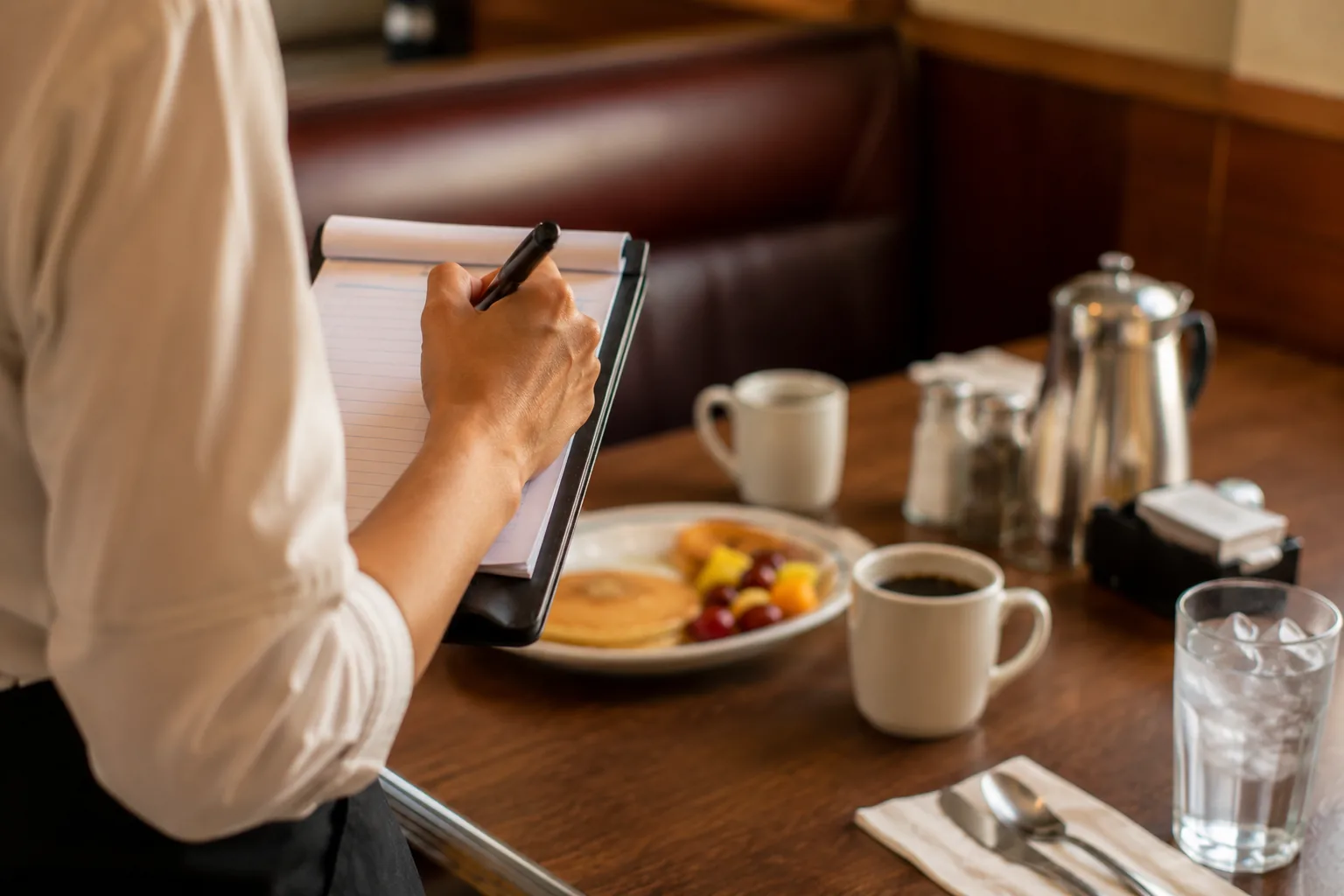 Server taking a breakfast order at a diner table, related to IHOP senior menu ordering
