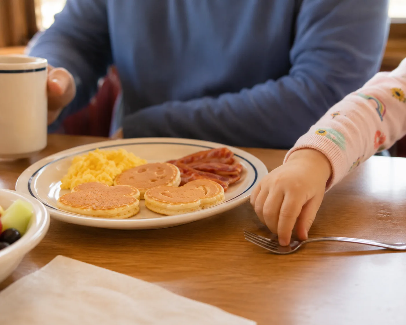 Child reaching for a fork at a diner table with a kids breakfast plate, related to IHOP kids menu